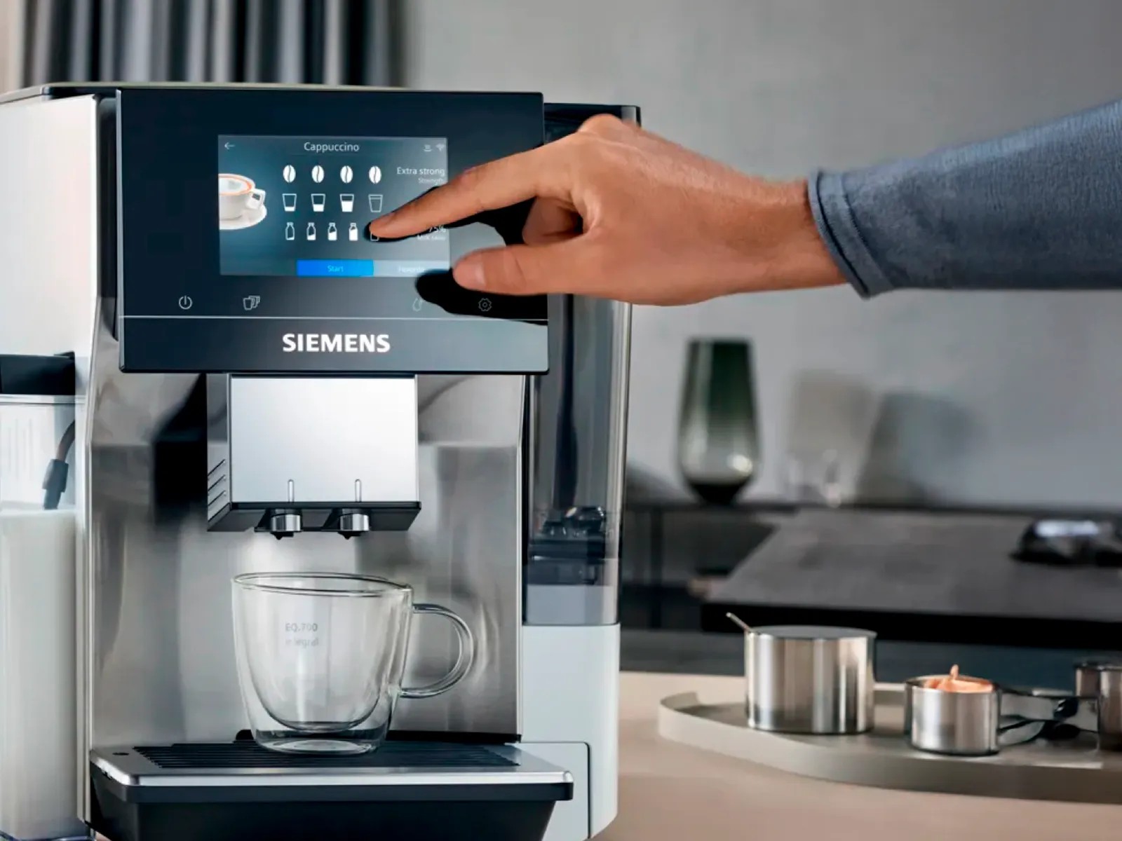 Person, der vælger cappuccino på en Siemens kaffemaskines touchskærm.