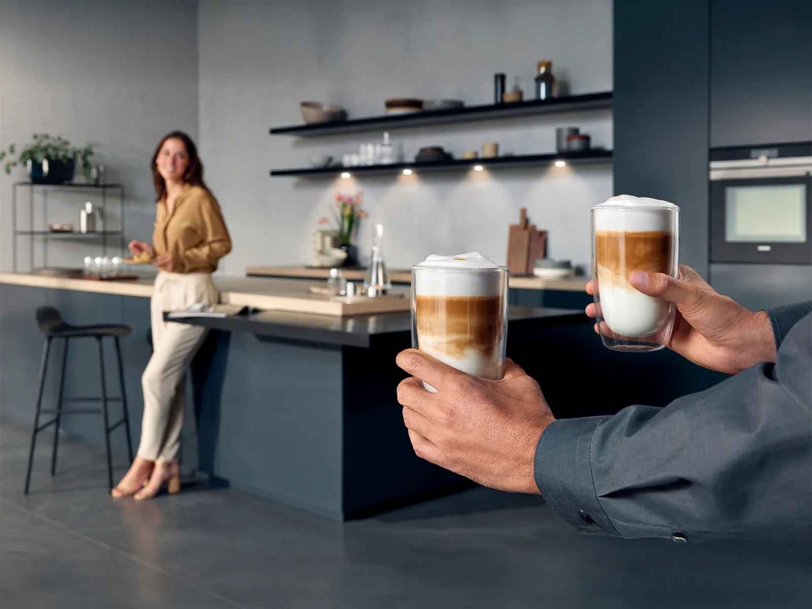 To hender som holder lagdelte kaffedrikker i et moderne kjøkkenmiljø.