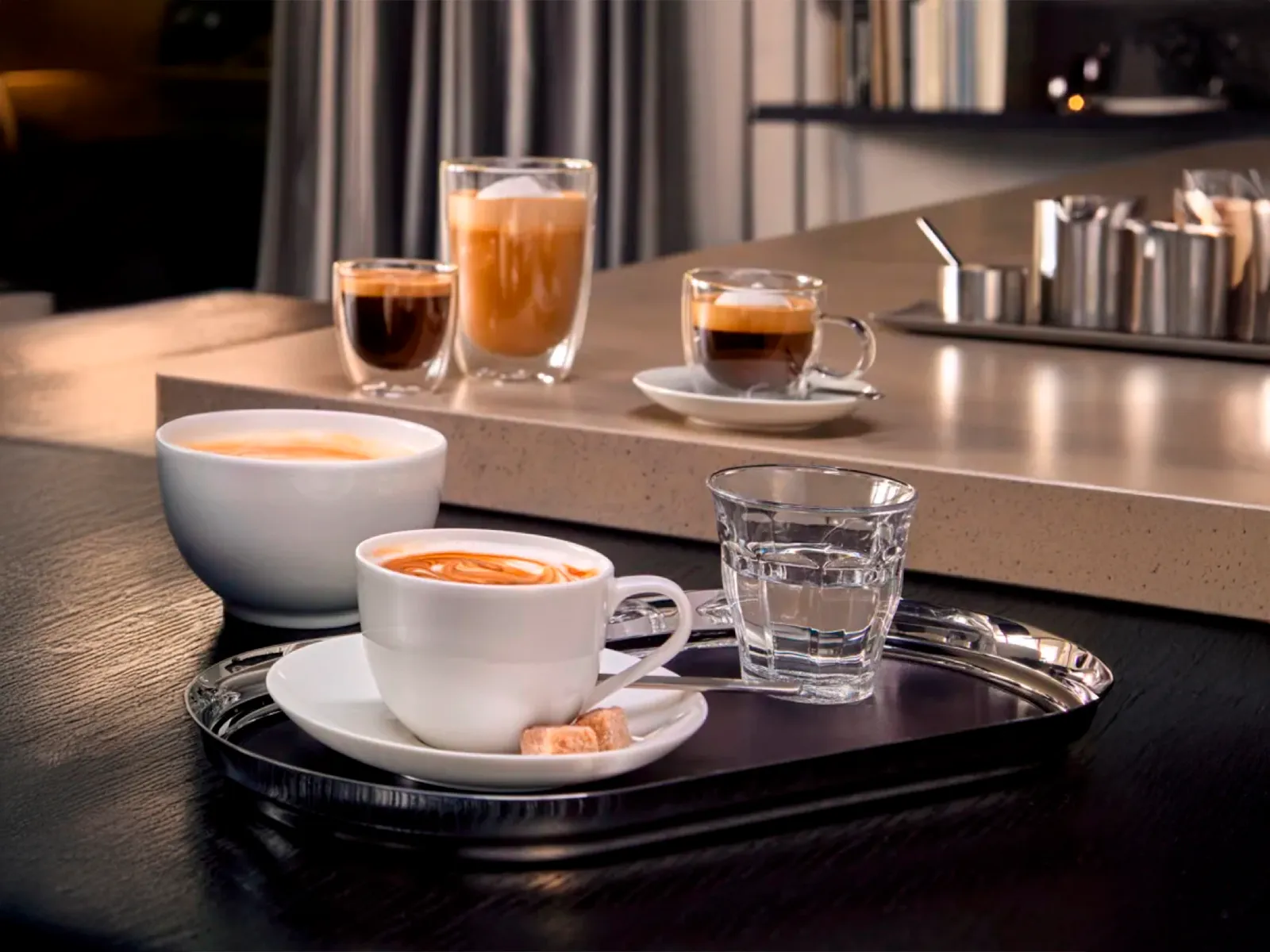 Forskellige kaffedrikke og et glas vand på en moderne køkkenbord.