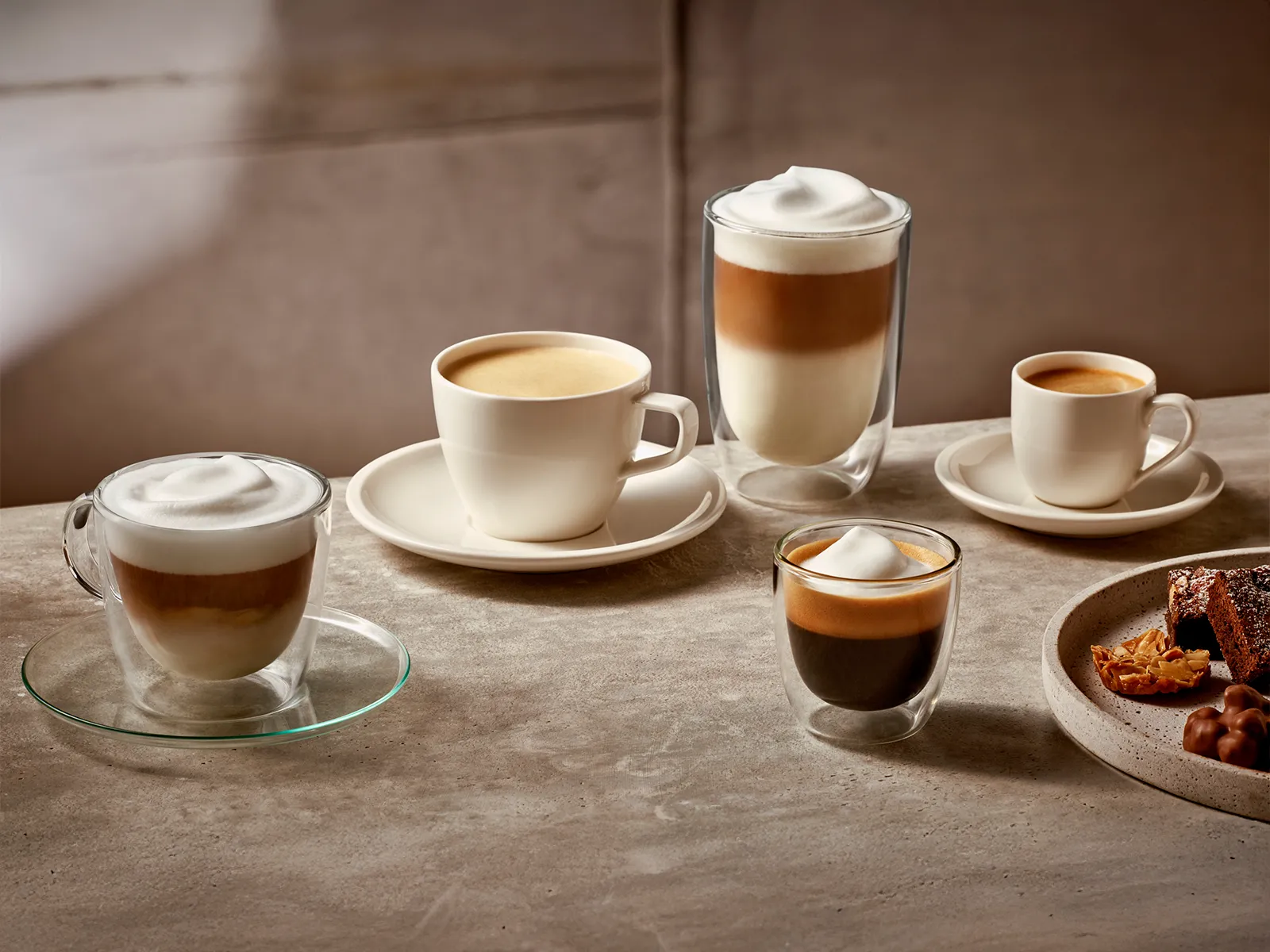 Varierede kaffedrikke på et bord, herunder en latte, cappuccino og espresso.