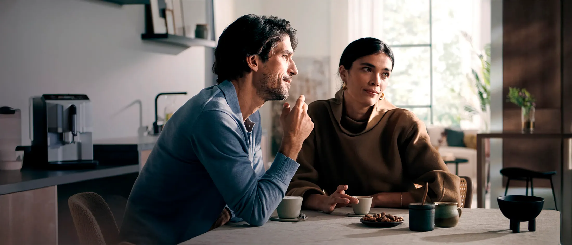 Two people enjoying coffee together in a modern kitchen, with a Siemens fully automatic coffee machine in the background.