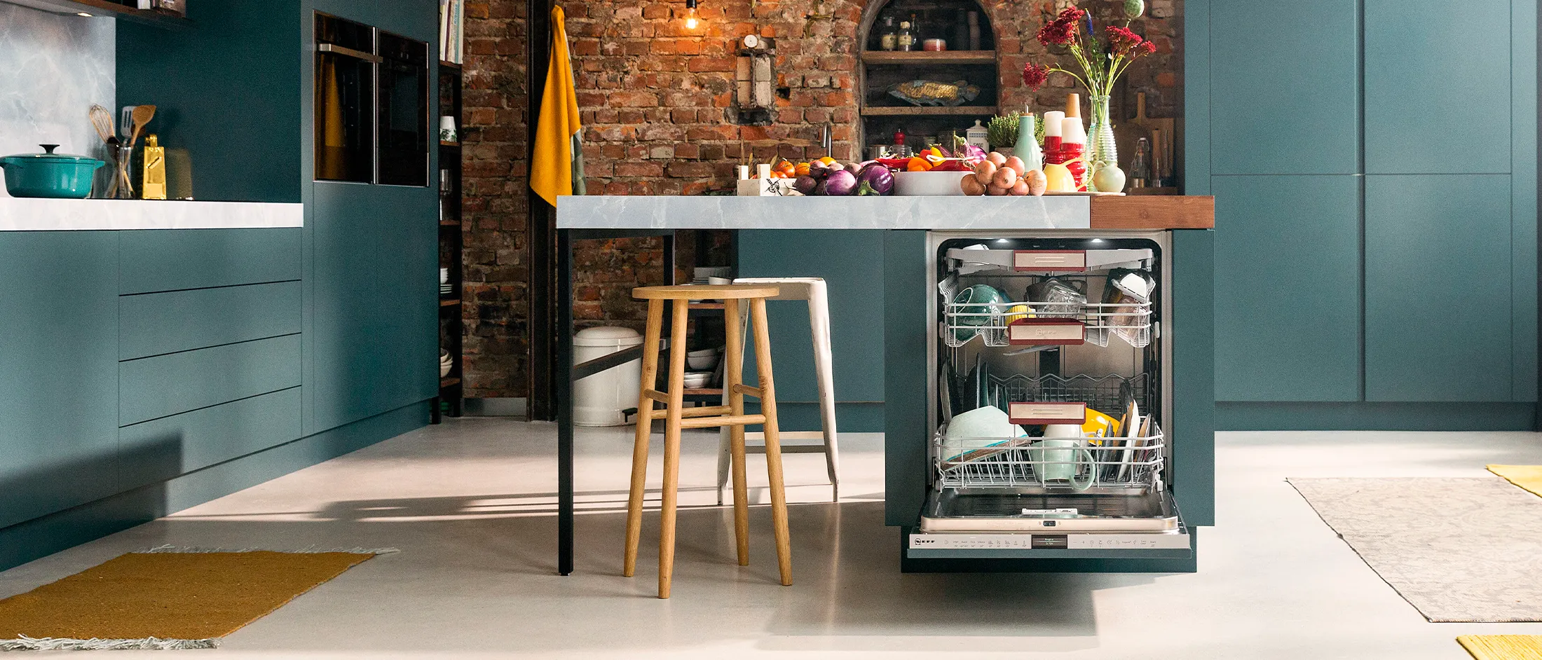 An industrial kitchen with an open dishwasher integrated in a kitchen island at the centre