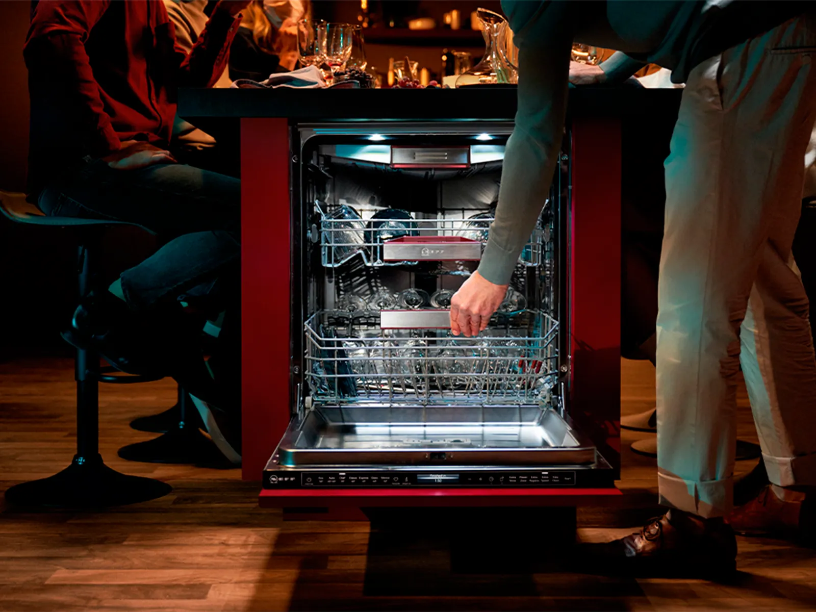 A person standing beside an open and illuminated dishwasher, pulling out the bottom basket