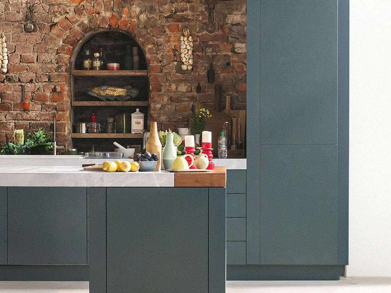 Modern kitchen with teal cabinets, exposed brick wall, and a wooden countertop with utensils.