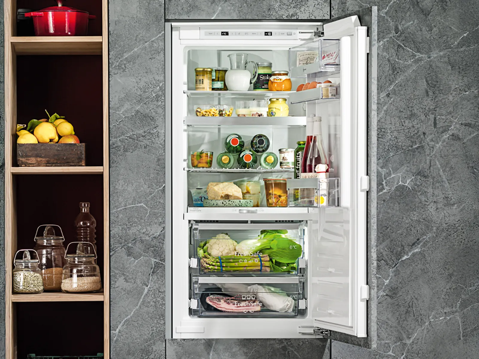 A modern refrigerator stocked with various food items, built into a kitchen unit with a gray marble backdrop.