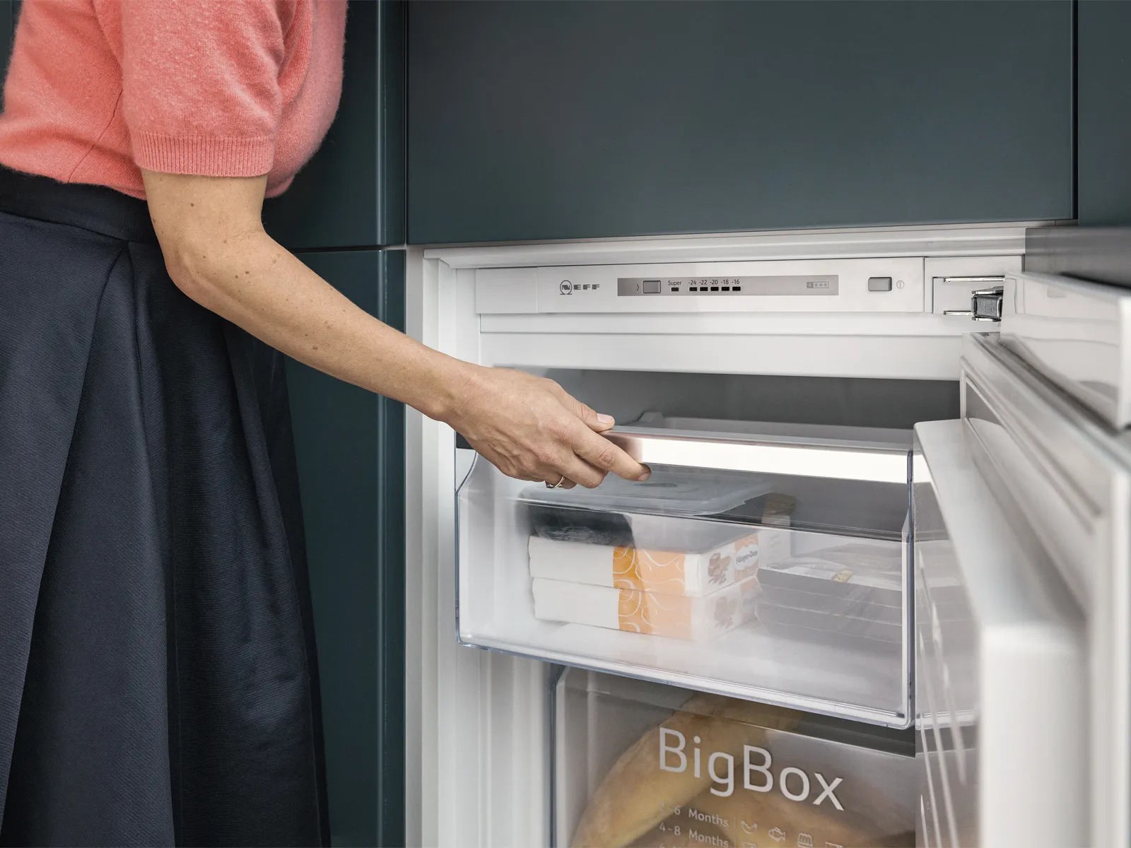 Une femme ouvre la porte du congélateur, révélant divers aliments à l'intérieur.
