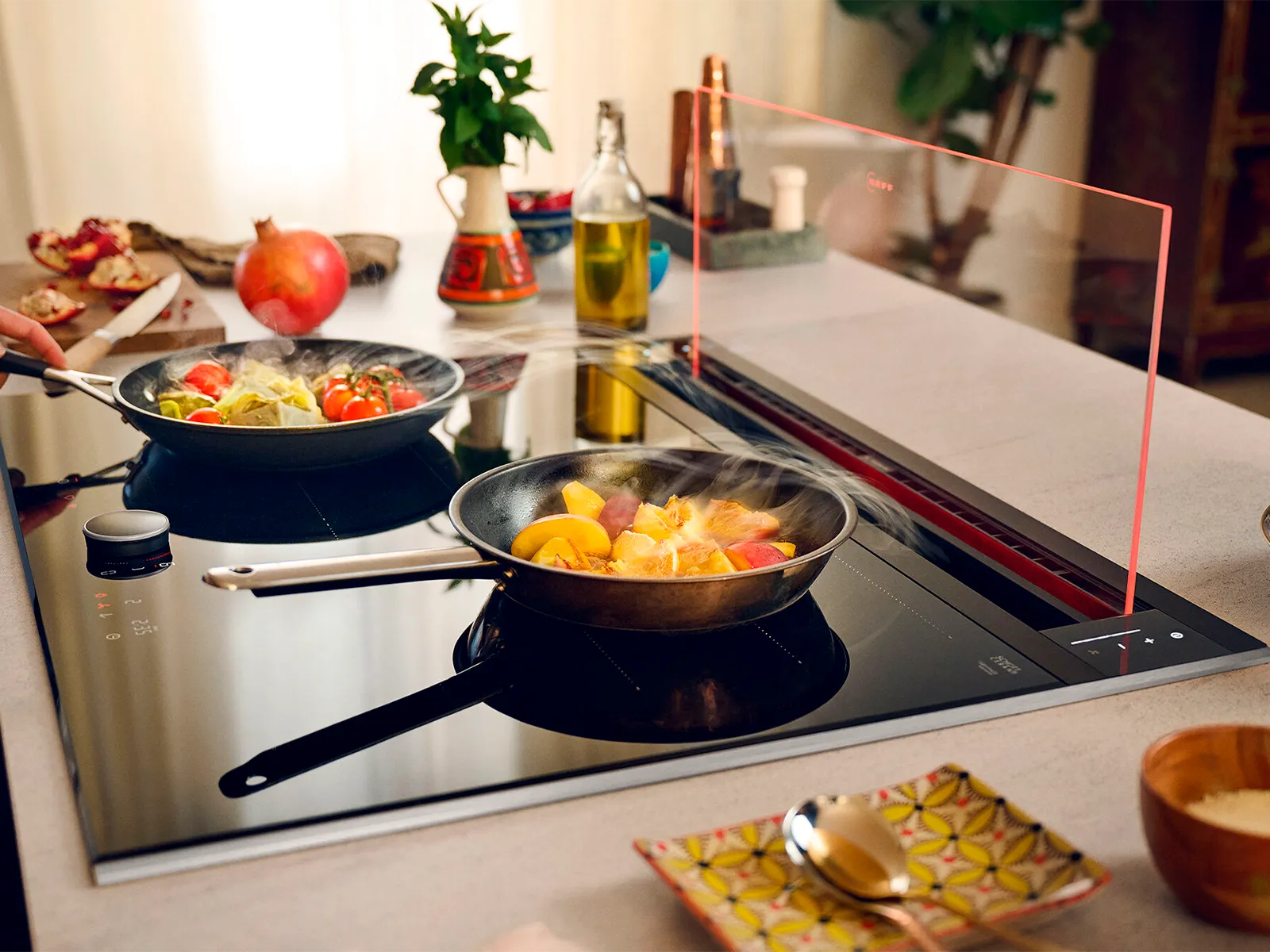 Glass draft hood shown with various dishes cooking on hob 