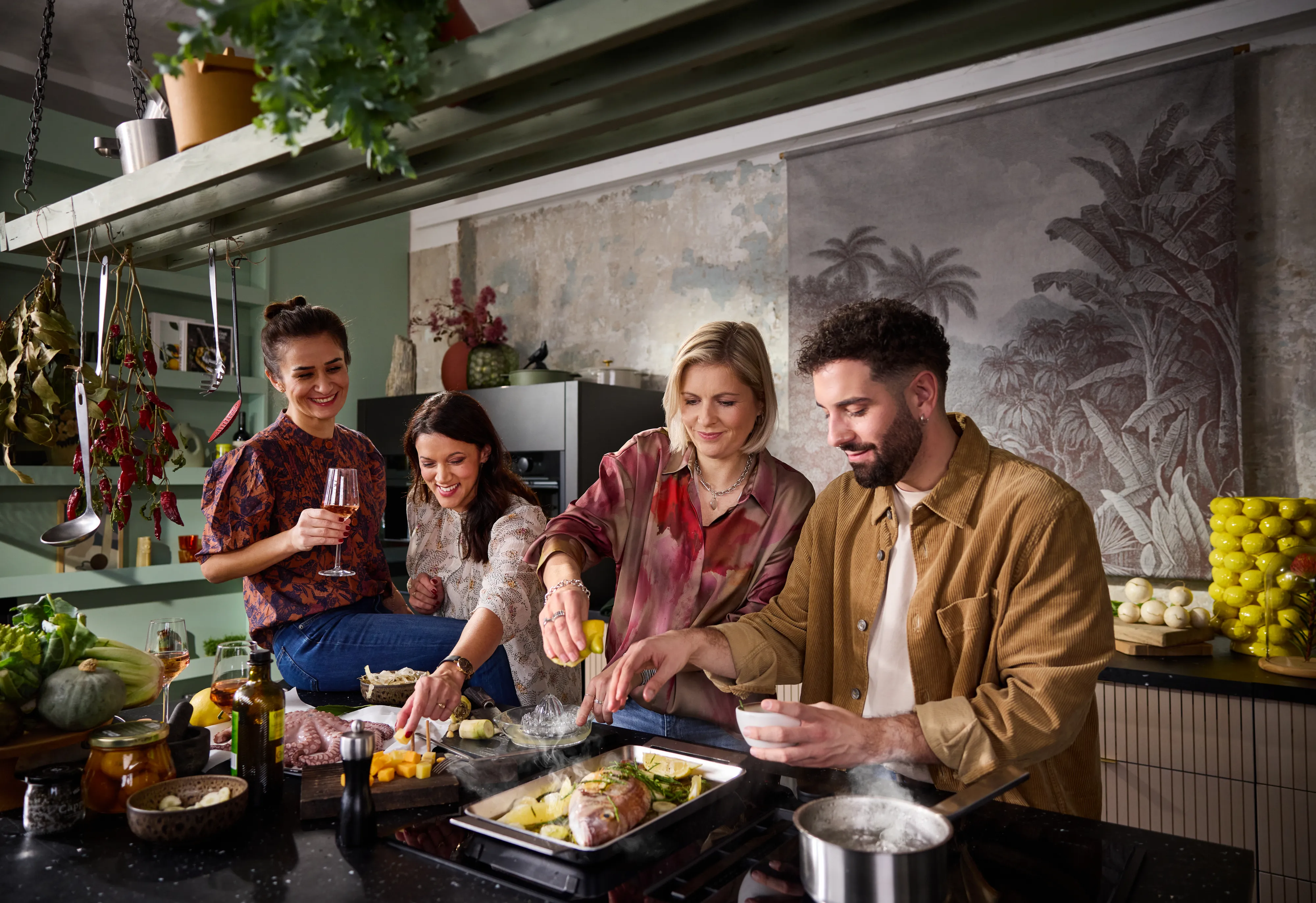Una cocina con un hombre de pie junto a una mujer que mezcla comida en un bol, mientras una mujer y otro hombre los observan desde detrás.