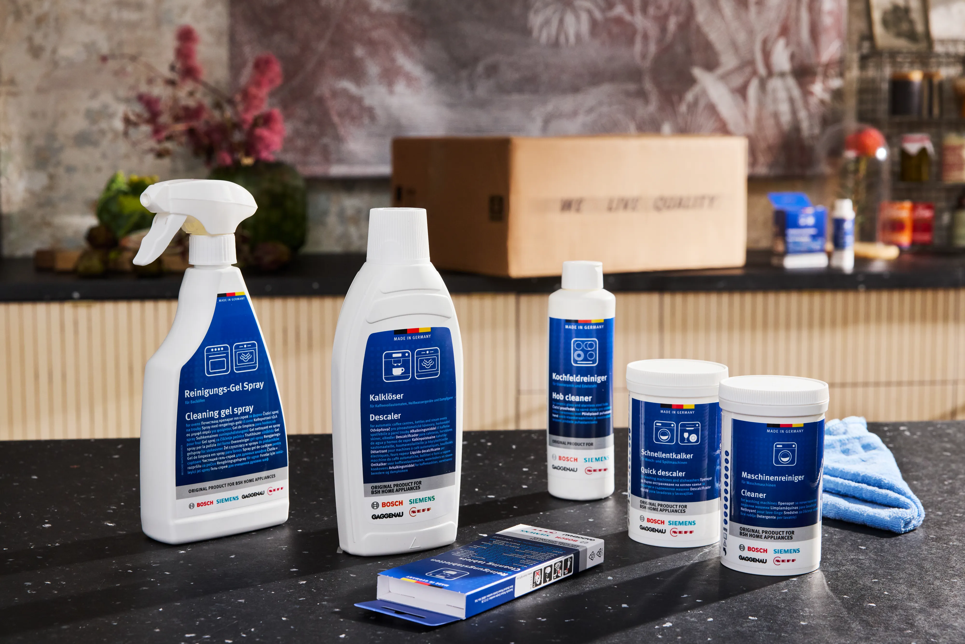 Groupe de produits d'entretien Bosch avec flacon pulvérisateur, bouteilles, pots et boîte sur un plan de travail en pierre.
