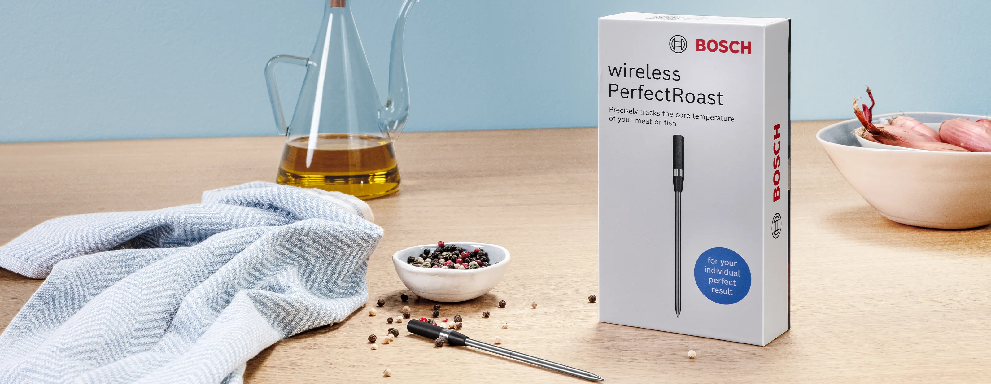 Produktverpackung des kabellosen Fleischthermometers Bosch „wireless PerfectRoast“ auf einem Holztisch neben Küchenutensilien.