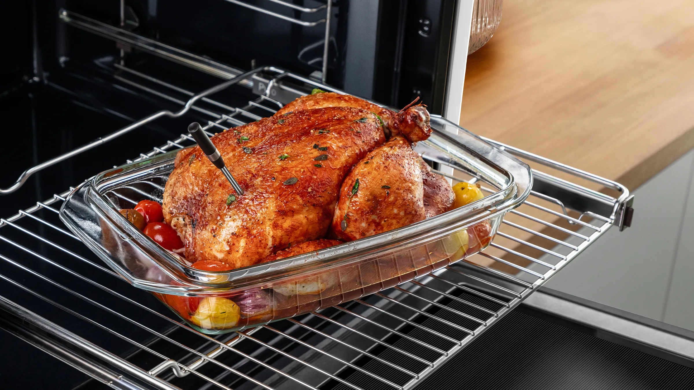Knuspriges Brathähnchen in einer Glasform auf dem ausgefahrenen Backofengitter eines Bosch-Backofens mit genutztem PerfectRoast Thermometer.