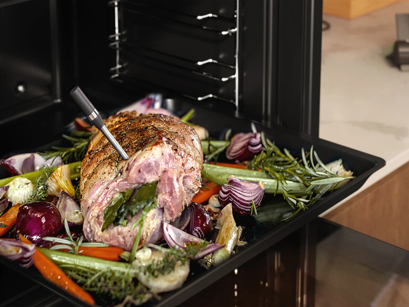 A roast in a NEFF oven, garnished with some vegetables besides of it and a wireless meatprobe in it.
