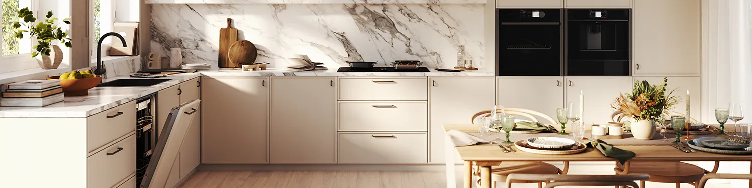 A panoramic view of a bright, contemporary kitchen with light-colored cabinets, a white marble backsplash, black integrated appliances, and a set dining table in the foreground.
