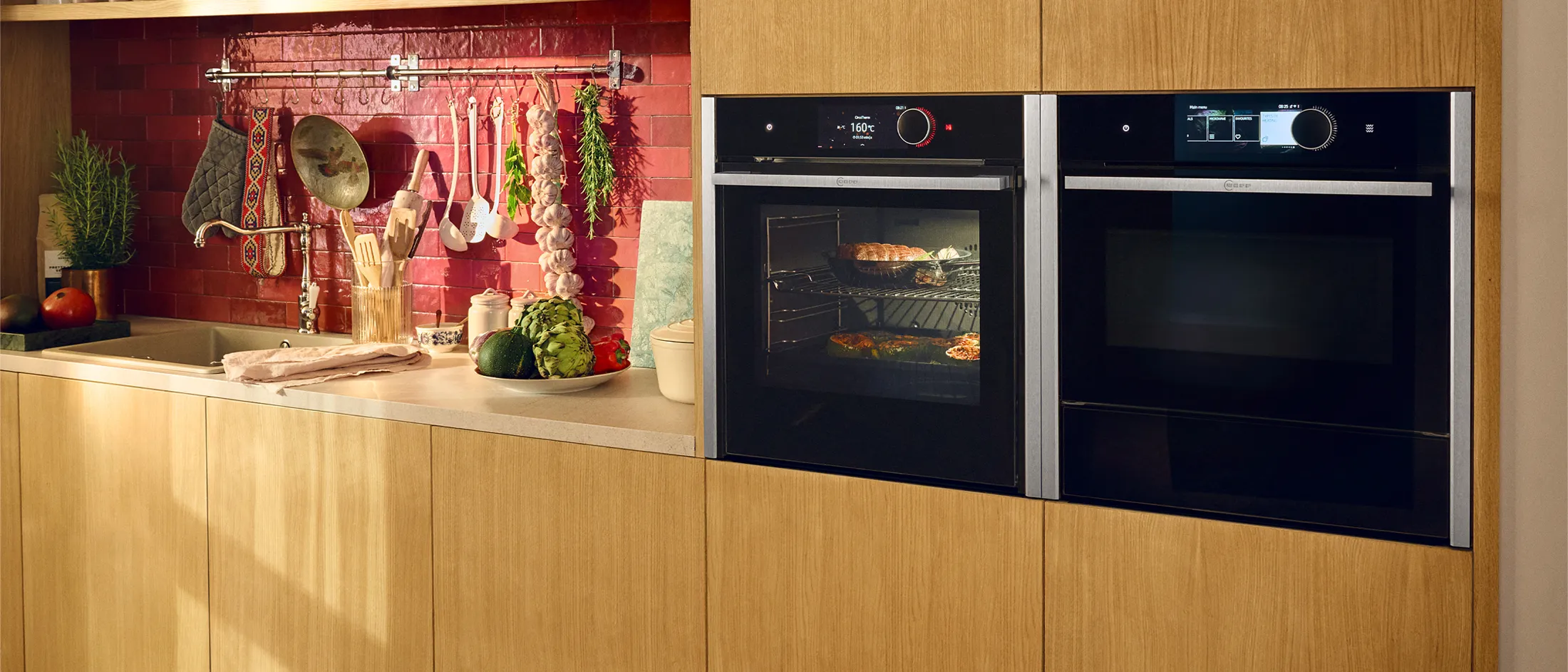 Two ovens in Metallic Silver shown side by side  in wooden kitchen with red tiles 