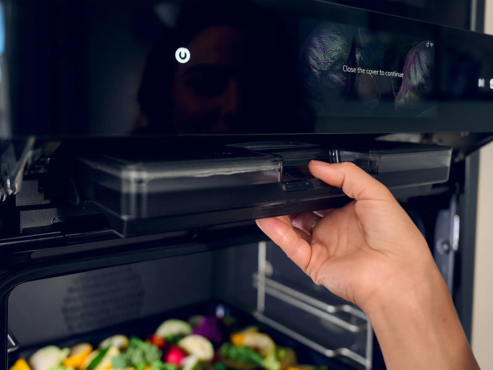 Hand removing steam water tank from oven, colourful vegetables seen in the oven cavity 