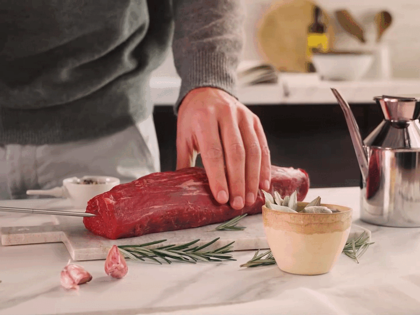 En person i en grå tröja förbereder en rå köttbit på en marmoriserad bänk genom att sätta in NEFF kötttermometern.