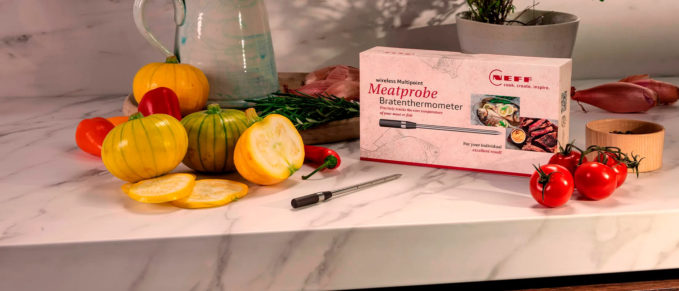 A meatprobe box rests on a marble countertop with colorful vegetables and herbs.