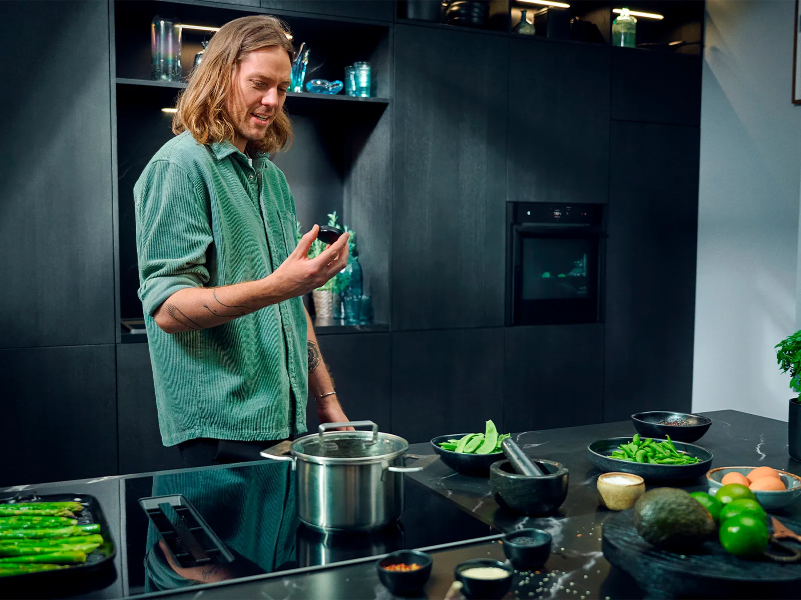 A man stands in a modern, dark kitchen in front of a hob with integrated ventilation and holds a Twist Pad Flex in his hand