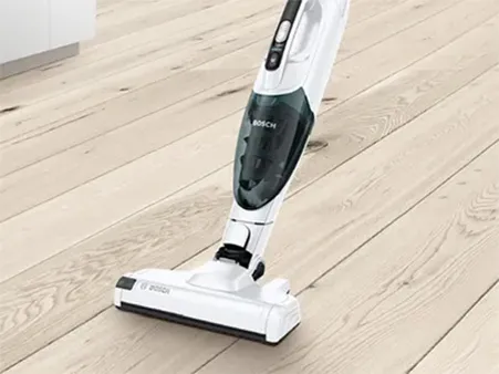 A Bosch cordless vacuum cleaner being used on a light wooden floor.