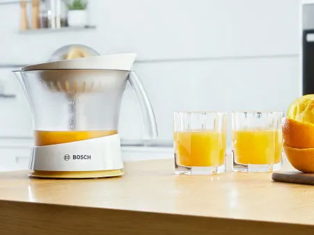 The Bosch citrus press VitaPress standing on a kitchen worktop with orange juice.