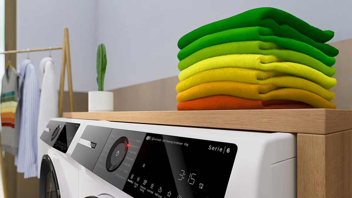Färgglada vikta kläder på trähylla, tvättmaskin i förgrunden.