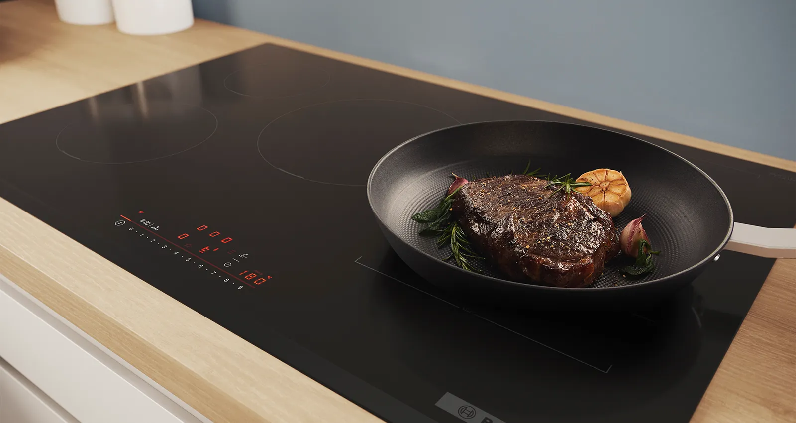 An Bosch induction hob with a pot of asparagus and steak in a pan.