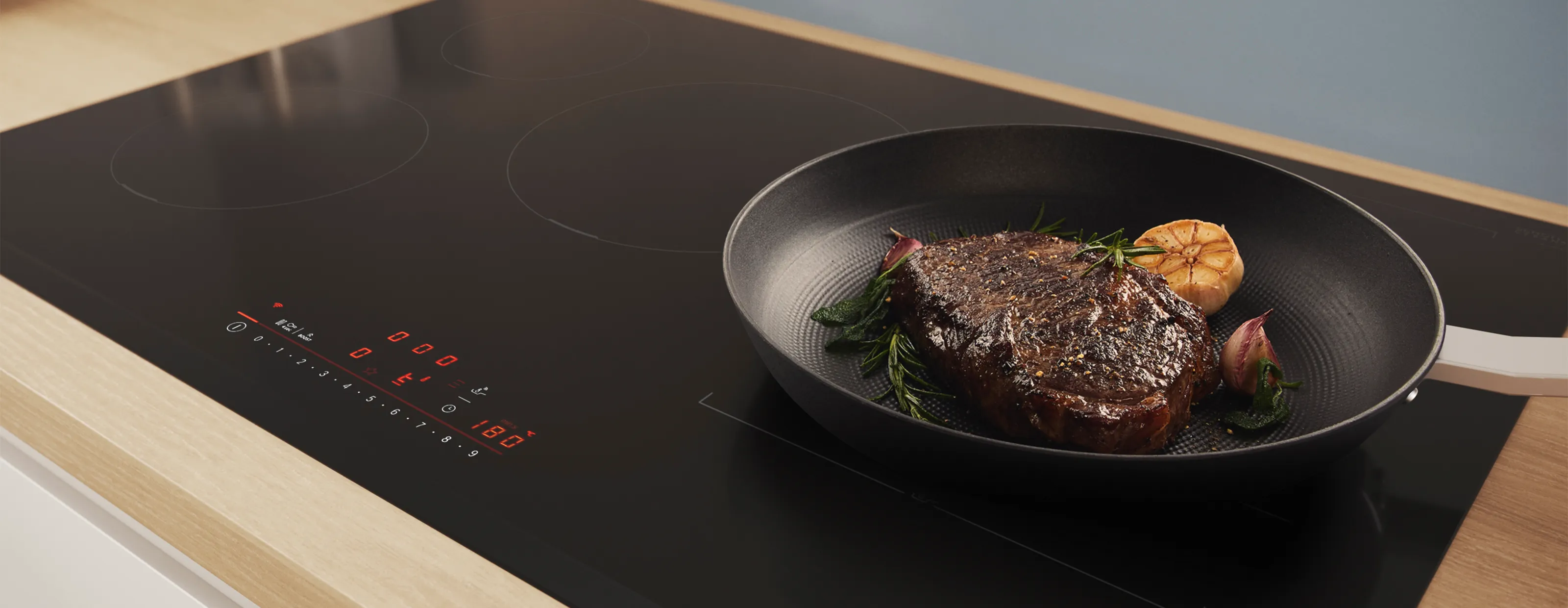 An Bosch induction hob with a pot of asparagus and steak in a pan.