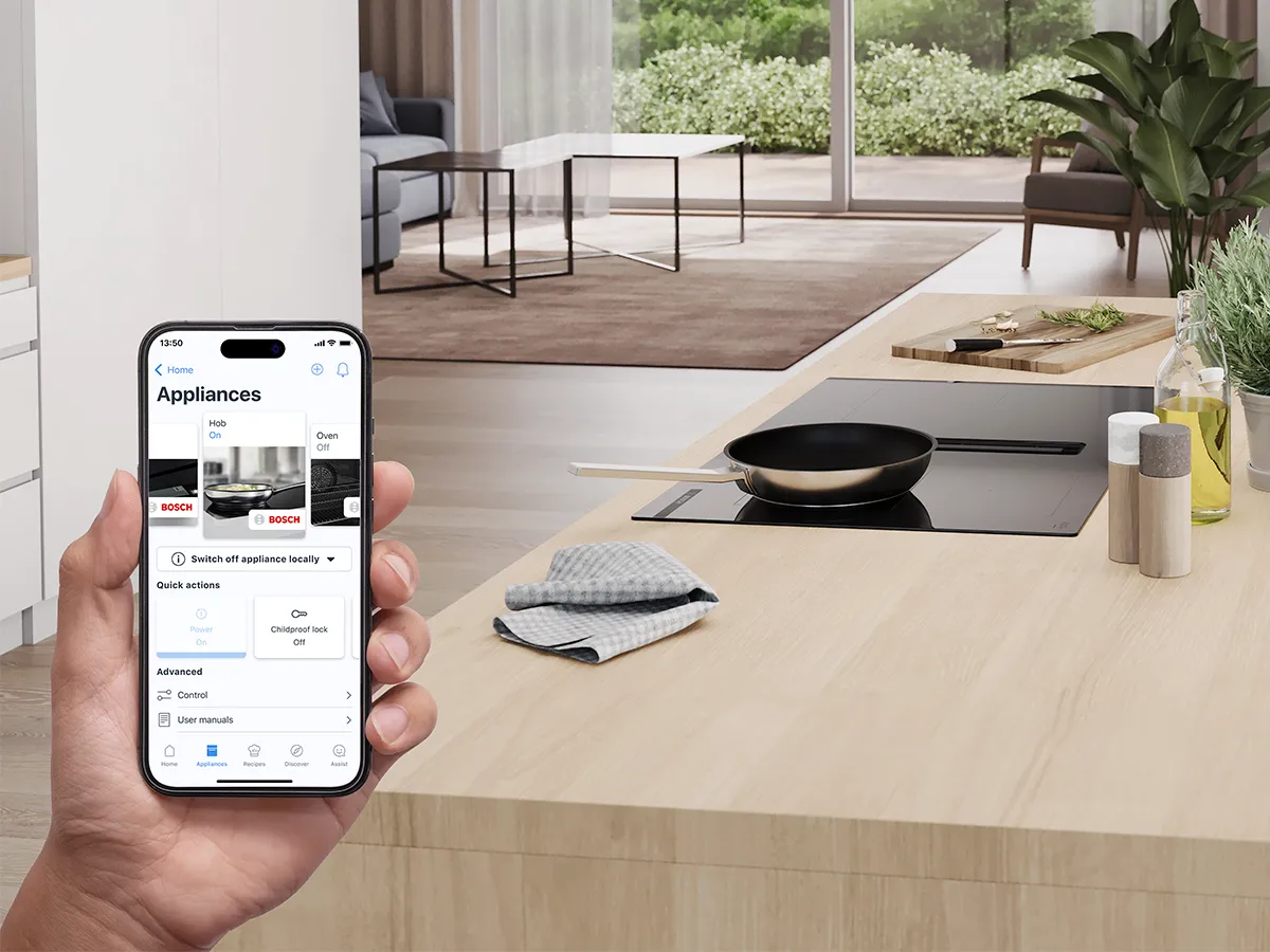 Person using home connect app with pan on hob in the background