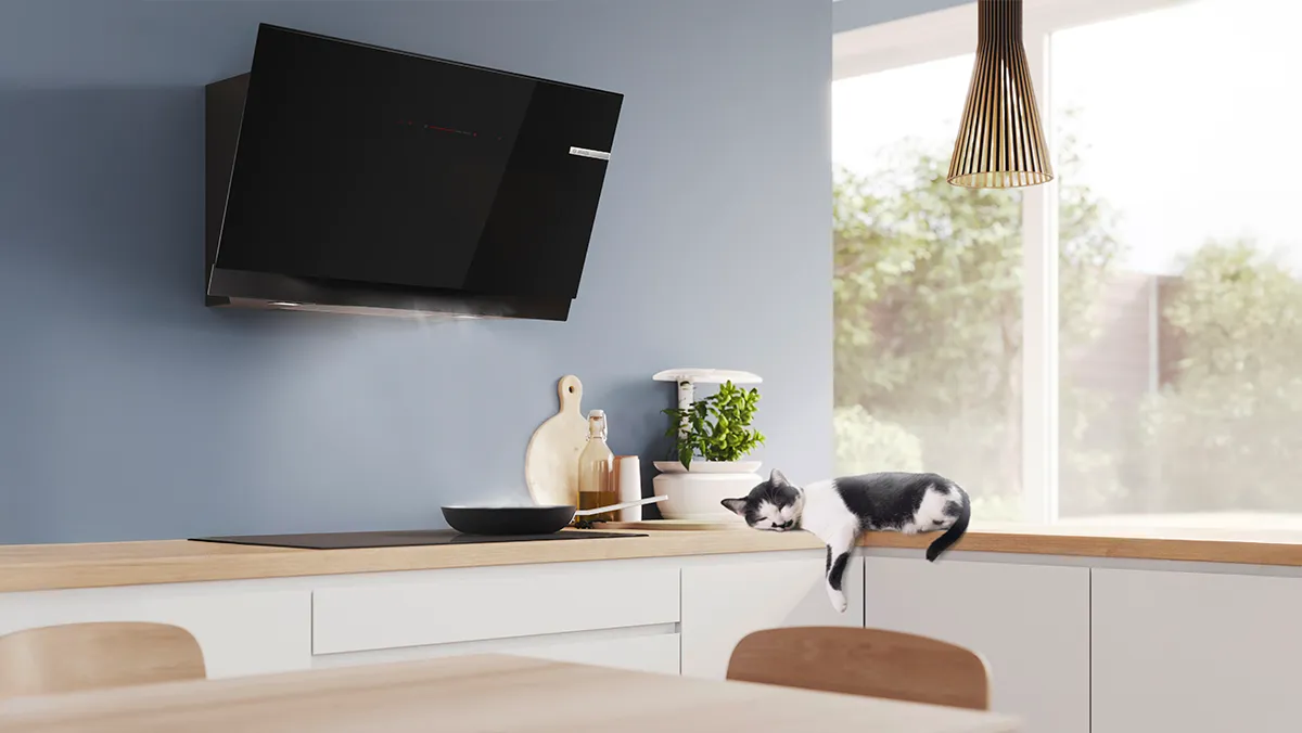 A sleek black kitchen hood hovers above a steaming pot, while a cat lounges on the countertop.