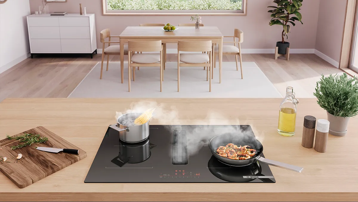 A modern kitchen, featuring boiling pasta and sizzling shrimp on an induction cooktop.
