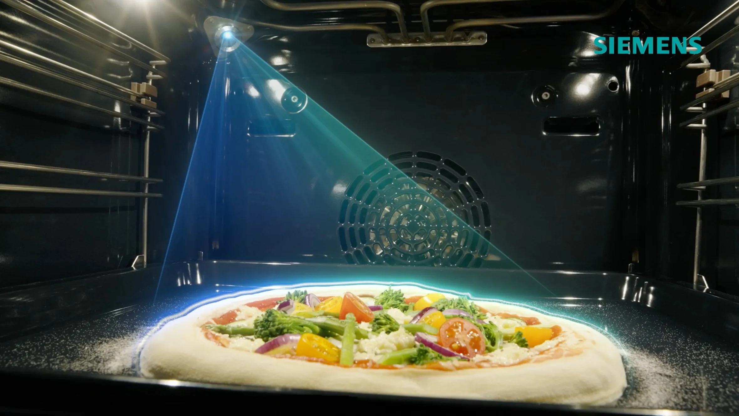 Fotocamera integrata con una luce blu simbolica che illumina una pizza all‘interno di un forno Siemens iQ700