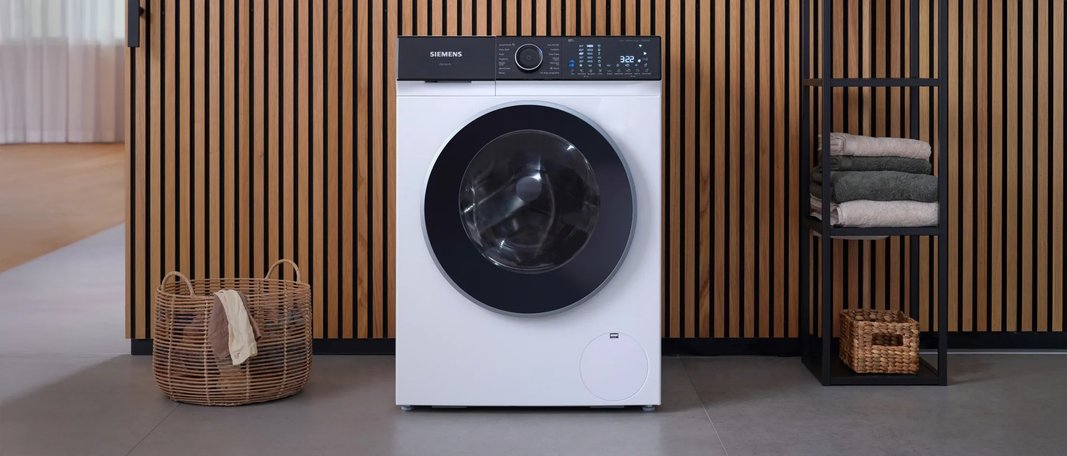 Máquina de lavar Siemens moderna numa sala com paredes de ripas de madeira e um cesto de roupa.