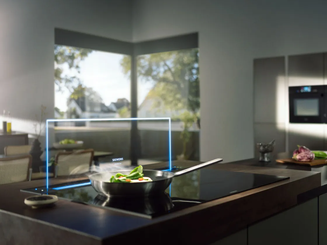 A hand holds an Apple Watch, positioned in front of a stylish kitchen, highlighting the blend of technology and home life.