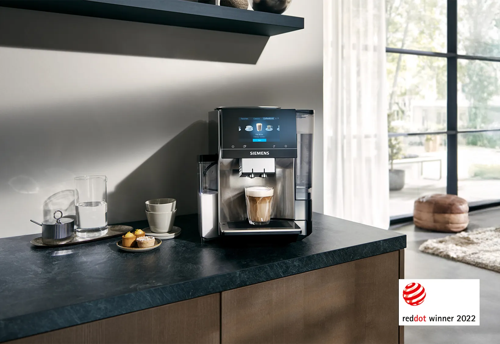 Moderne Siemens kaffemaskine på køkkenbordet med en frisk kop kaffe, snacks og Red Dot Winner 2022-logoet.