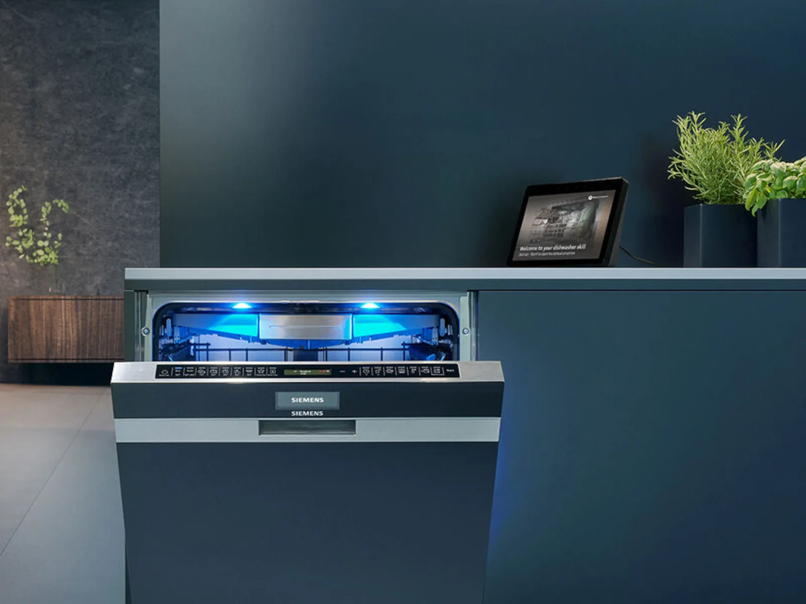 A Siemens dishwasher with a blue interior light, slightly open, beside a tablet.