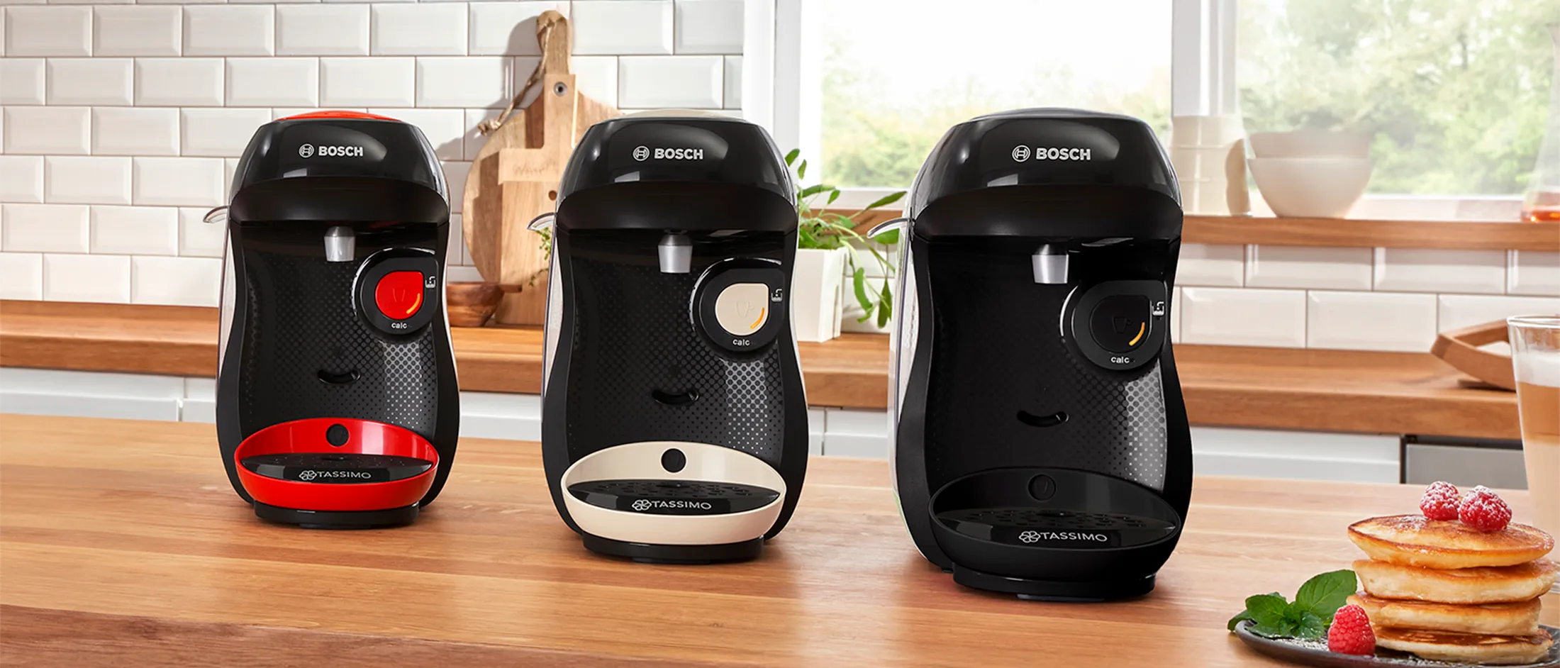 TASSIMO HAPPY friendly coffee makers in different colours on a kitchen worktop.