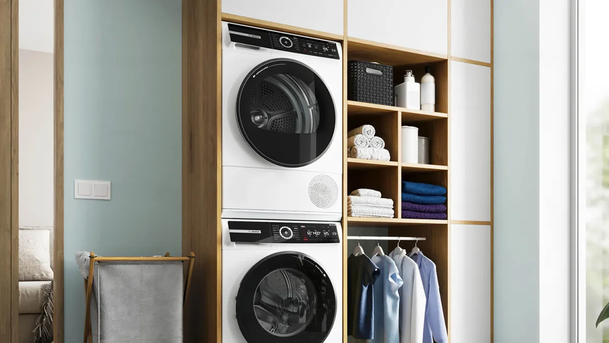 Ein moderner Waschbereich mit einer gestapelten Waschmaschine und einem Trockner sowie einem Holzregal, das ordentlich gefaltete Handtücher und Kleidung zeigt.