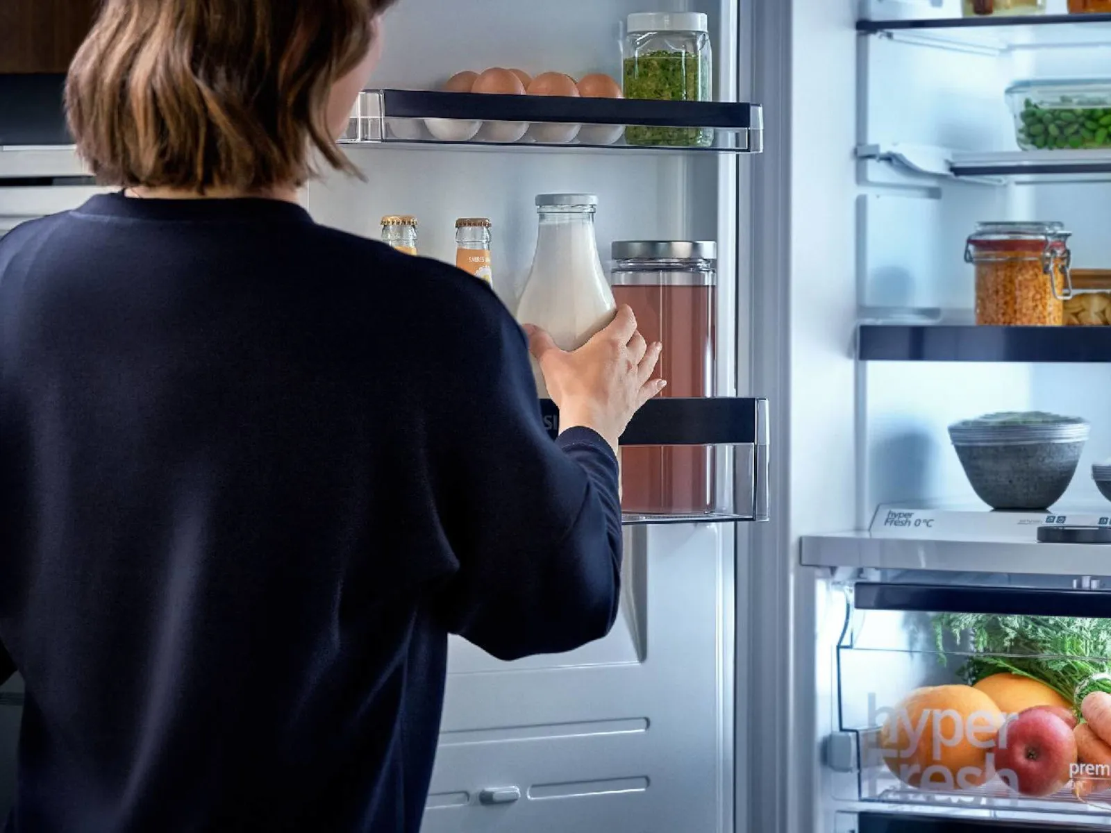 A person reaches for a milk bottle in a modern refrigerator.