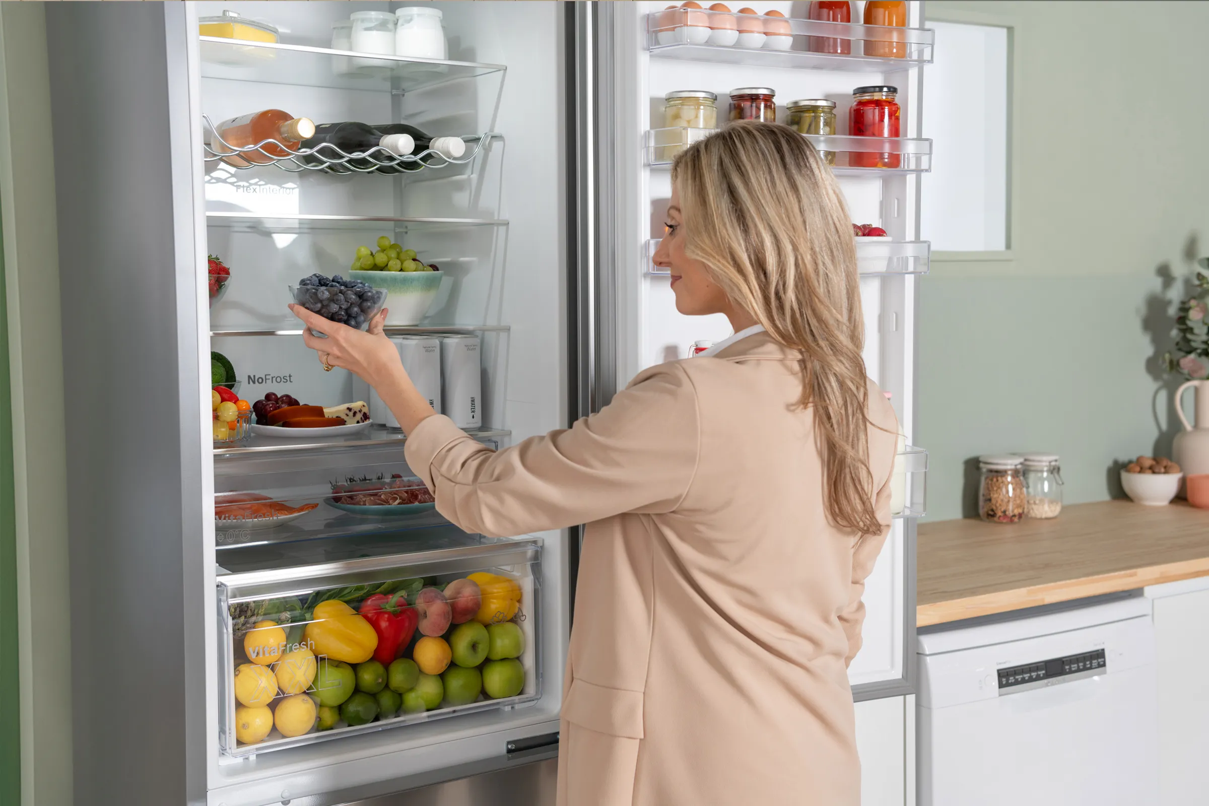 A woman stands in a kitchen, gazing thoughtfully at an open refrigerator filled with various food items.  