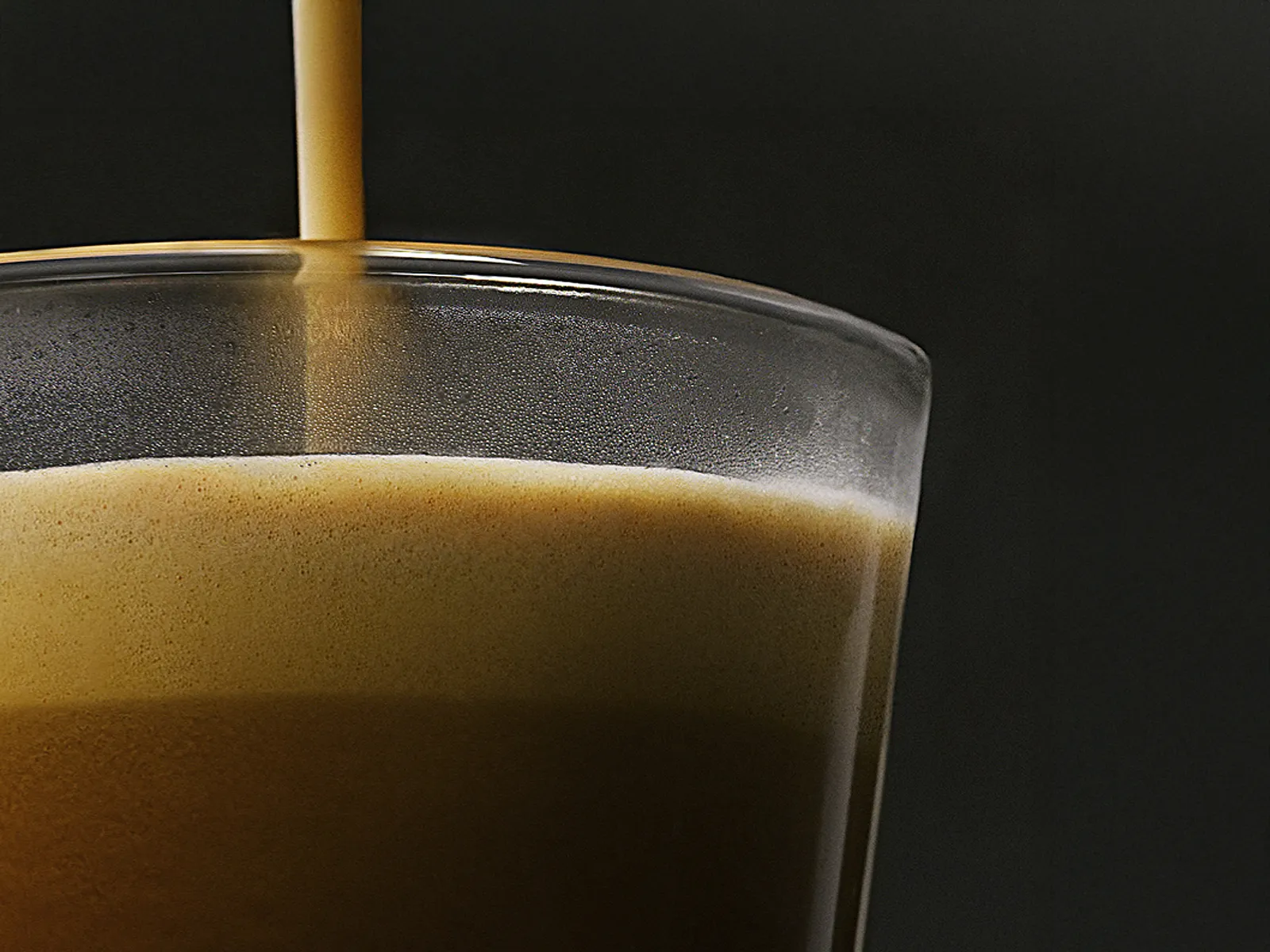 Prim-plan al unei creme de espresso catifelate într-un pahar transparent.