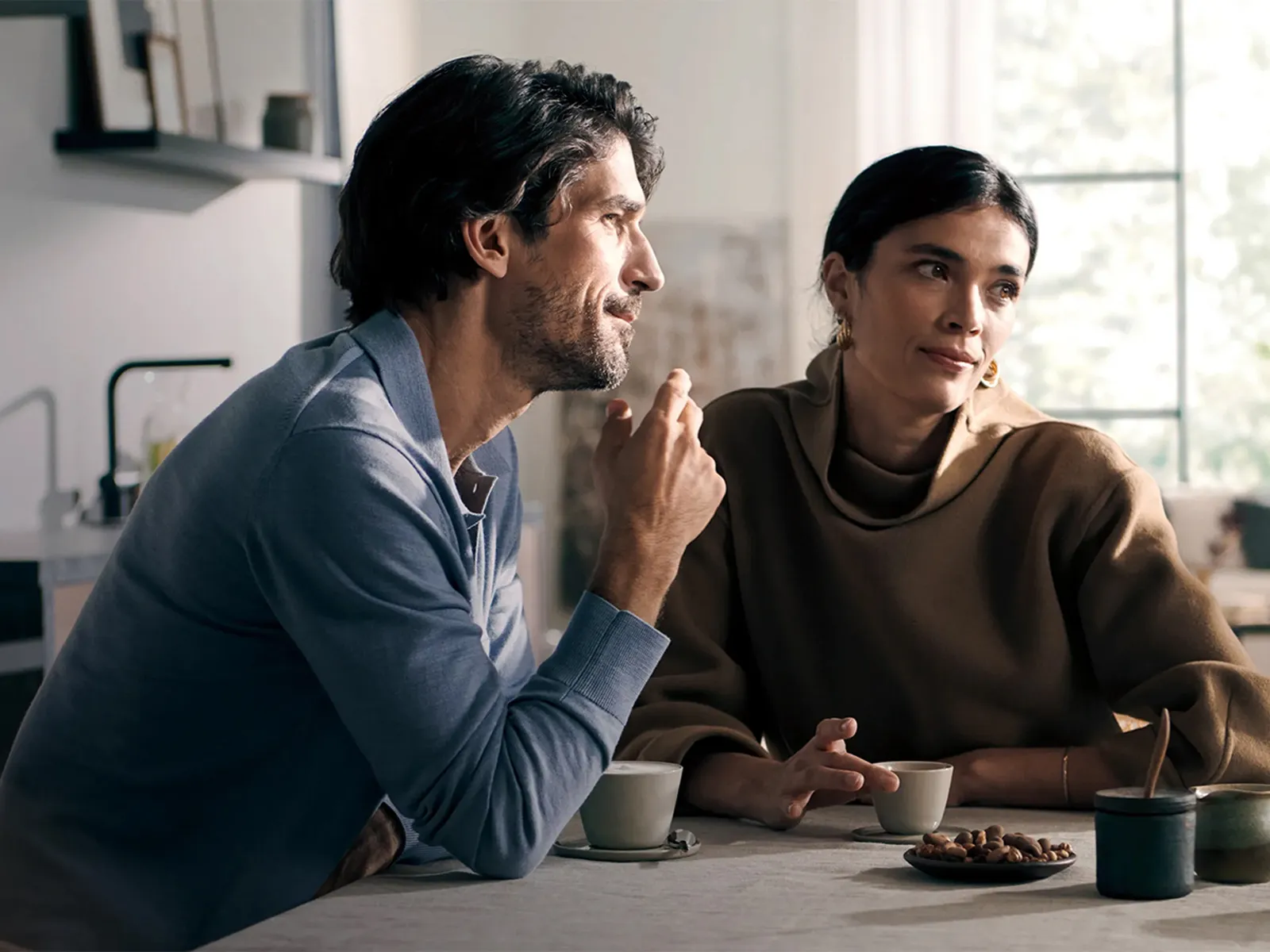 Două persoane savurând cafeaua împreună într-o bucătărie modernă, cu un espressor automat Siemens în fundal.