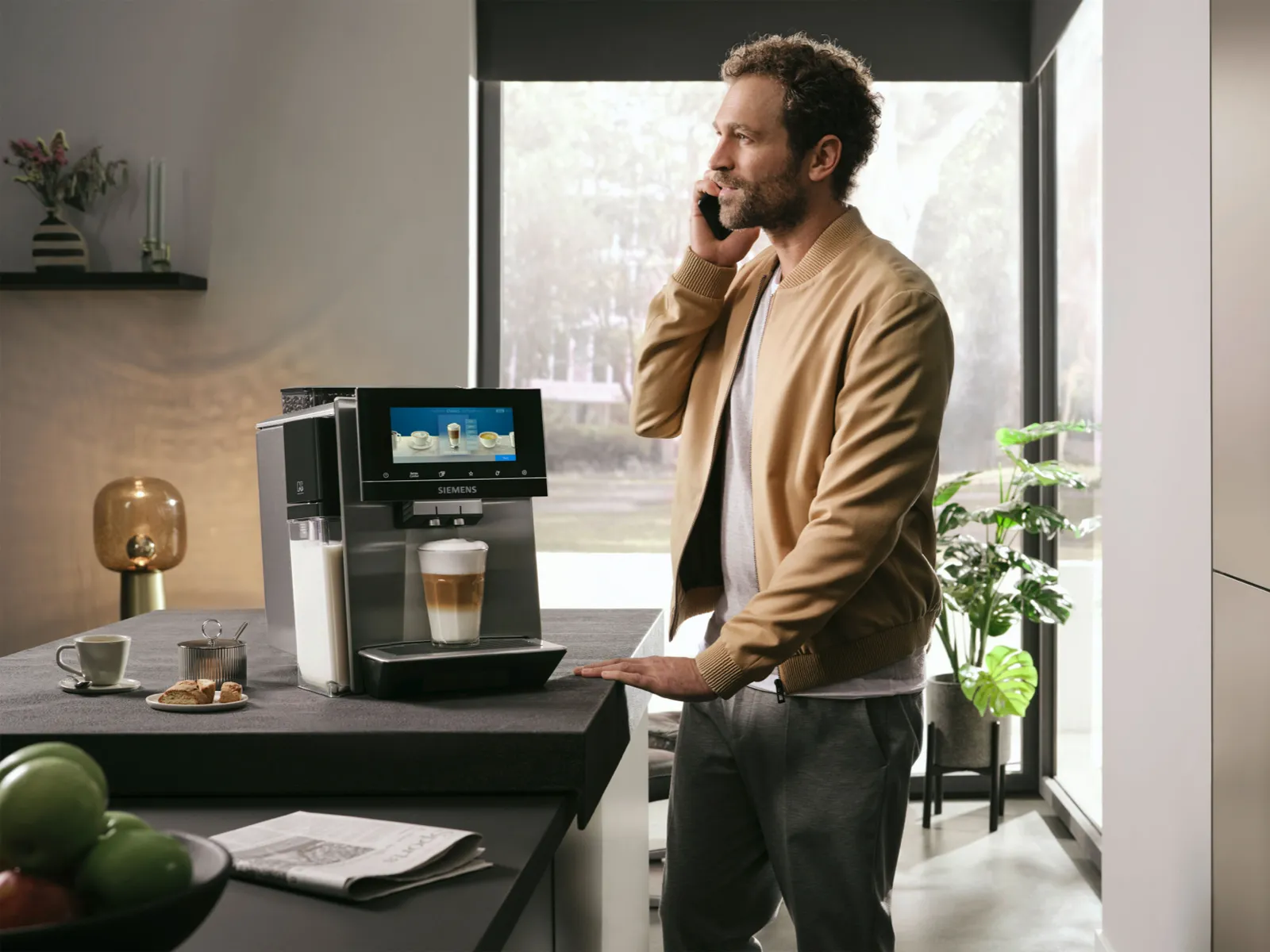 Un bărbat de aproximativ 35 de ani folosește un espressor automat superSilent de la Siemens în timp ce poartă o conversație la telefon.