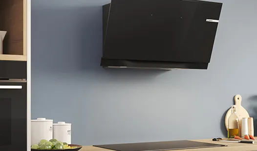 Moderne Küche mit einer eleganten schwarzen Dunstabzugshaube über einer minimalistischen Arbeitsplatte, daneben kleine weiße Vorratsbehälter und ein Schneidebrett.