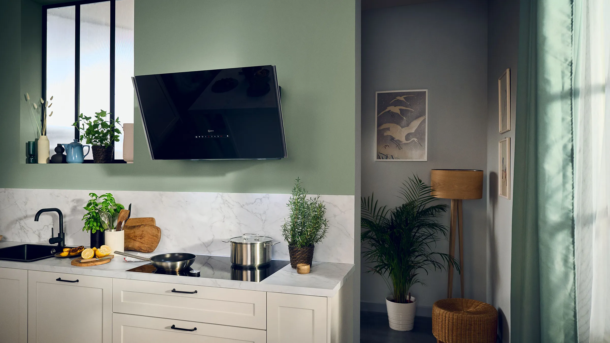 Modern kitchen with white cabinets, black appliances, plants, and artwork on the wall.