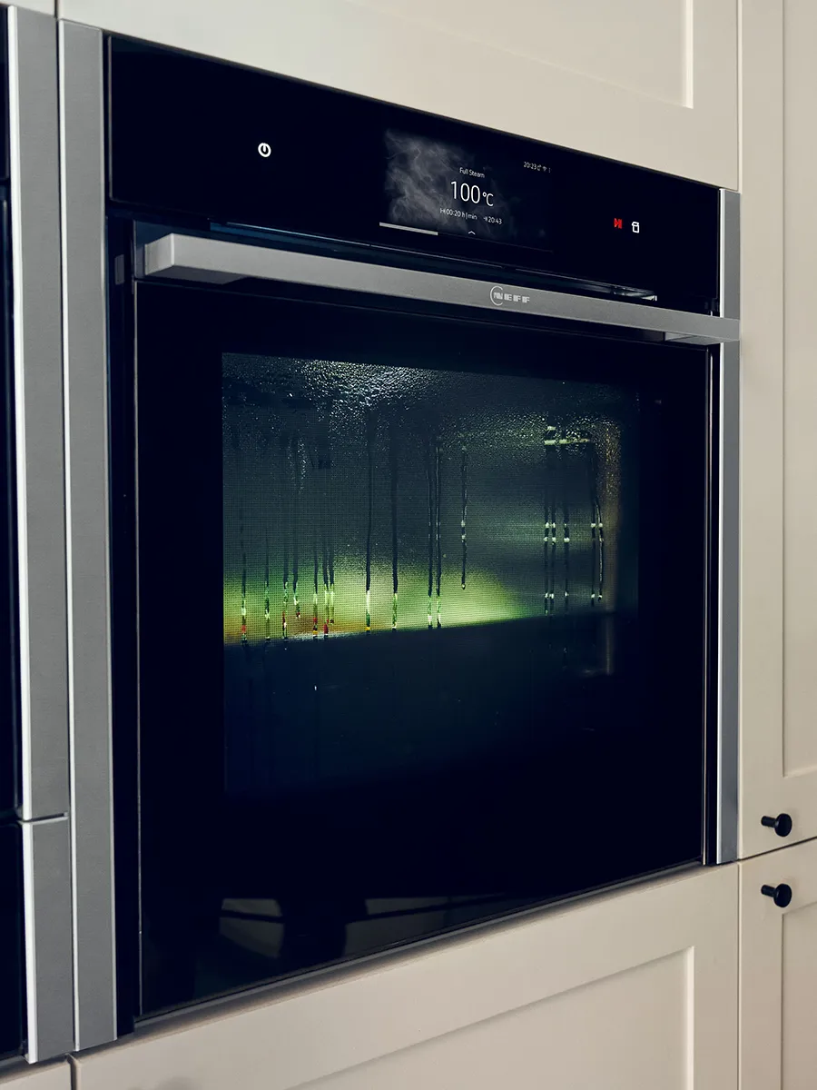A close-up of a black NEFF built-in oven during a steam cooking cycle. The glass door is covered in condensation, obscuring the food inside. The digital display above reads "Full Steam" at "100°C".