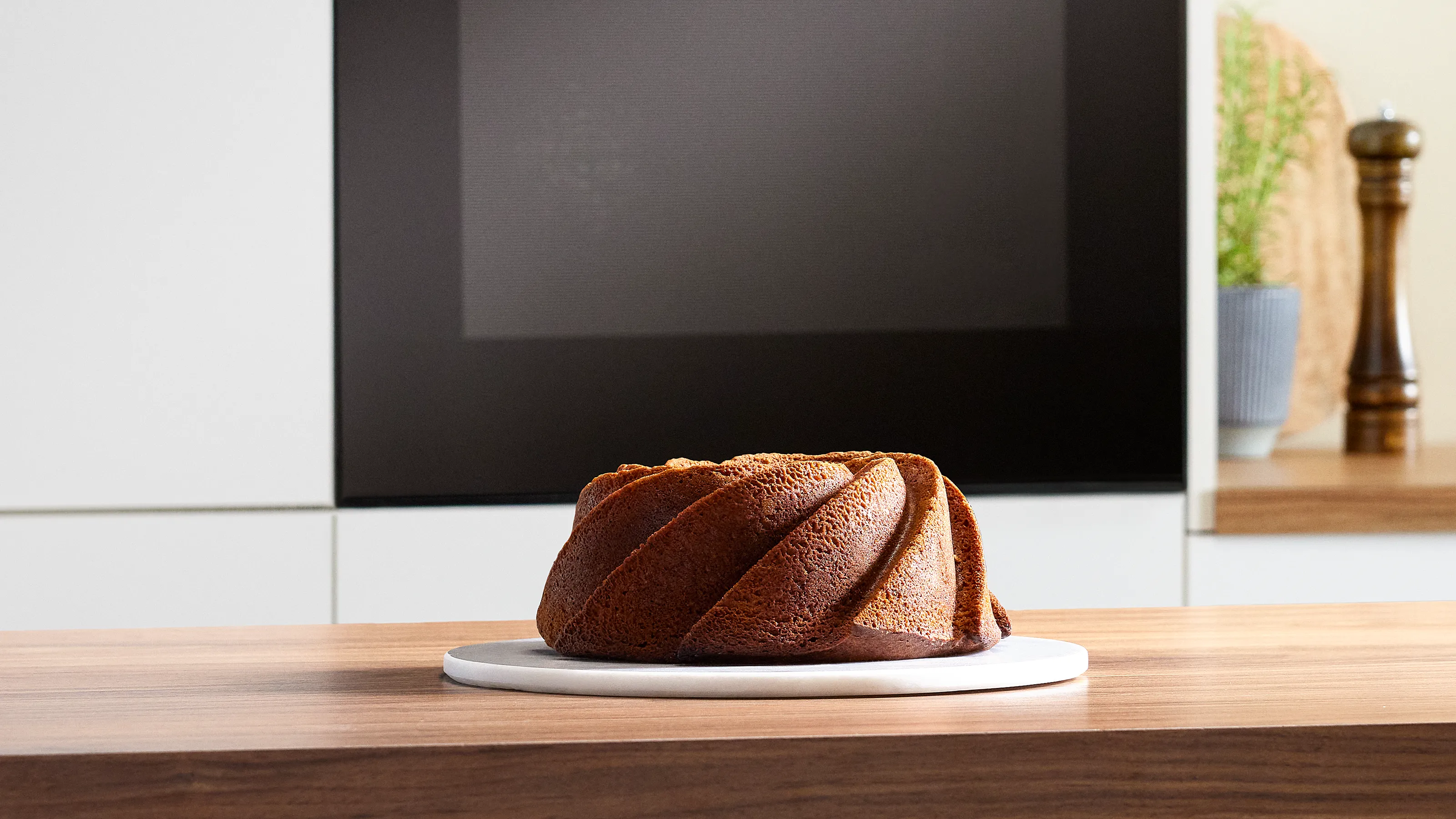 Bundt pastası ahşap masada, mutfak aleti arka planda, minimalist dekorasyon.