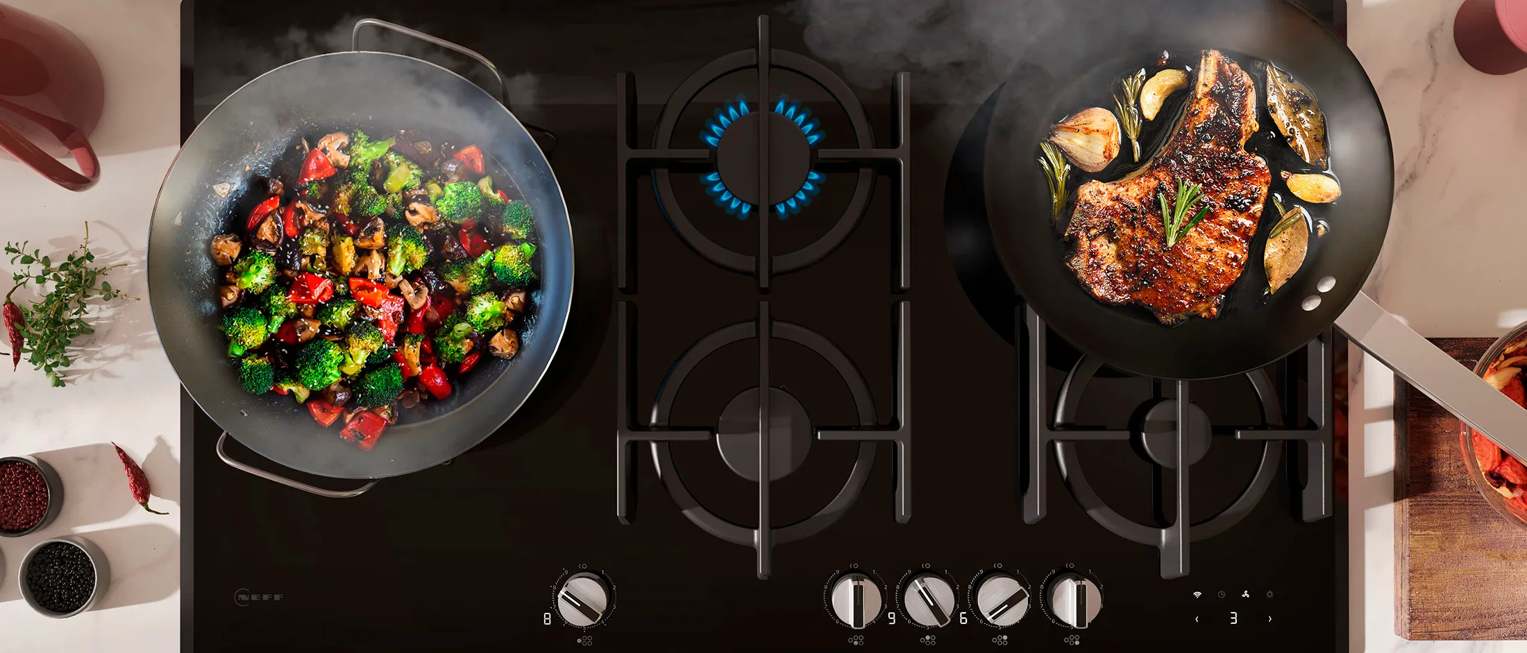 Une plaque de cuisson à gaz noire avec des légumes dans une poêle et un steak poêlé dans une autre.