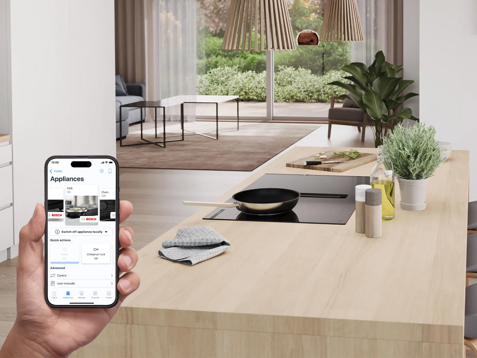 Modern kitchen with induction cooktop on an island. Person holding smartphone showing app.