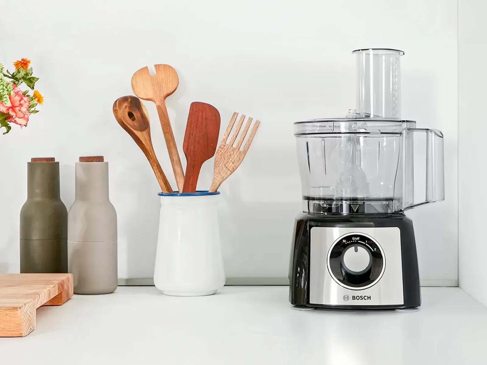 Un robot de cuisine posé à côté des ustensiles, du sel et du poivre sur un plan de travail.