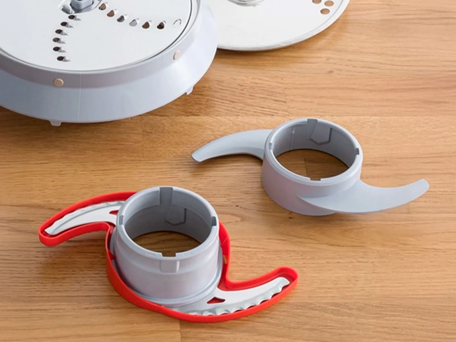 Pièces d’assemblage d’un appareil de cuisine, avec des lames Supercut grises et un anneau rouge, posées sur une surface en bois.